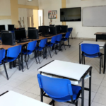 Sala 201 – Sala de Sistemas de alta calidad de la Institución Educativa John F. Kennedy: espacio amplio y organizado con aproximadamente 35 computadores de escritorio dispuestos en filas, mesas y sillas azules para estudiantes, tablero y pantalla al frente, iluminación natural y artificial, destinado al desarrollo de actividades de informática y profundización en sistemas.