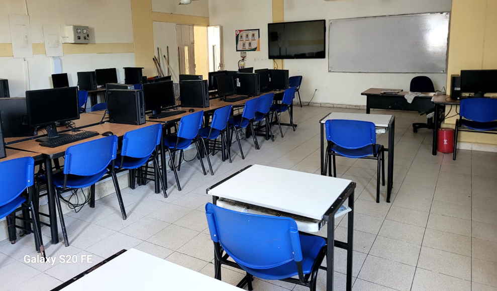 Sala 201 – Sala de Sistemas de alta calidad de la Institución Educativa John F. Kennedy: espacio amplio y organizado con aproximadamente 35 computadores de escritorio dispuestos en filas, mesas y sillas azules para estudiantes, tablero y pantalla al frente, iluminación natural y artificial, destinado al desarrollo de actividades de informática y profundización en sistemas.