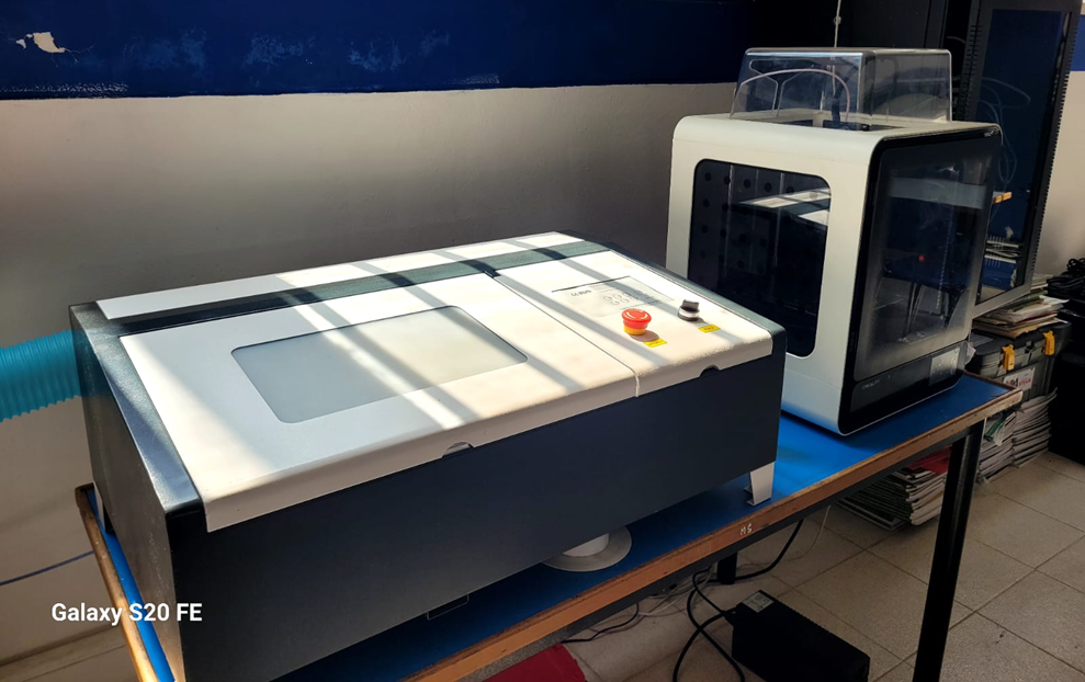 Sala de Robótica – equipos especializados: área de trabajo con cortadora láser e impresora 3D, ubicadas sobre mesas técnicas, destinadas al diseño, prototipado y fabricación de piezas para proyectos de robótica e innovación educativa.