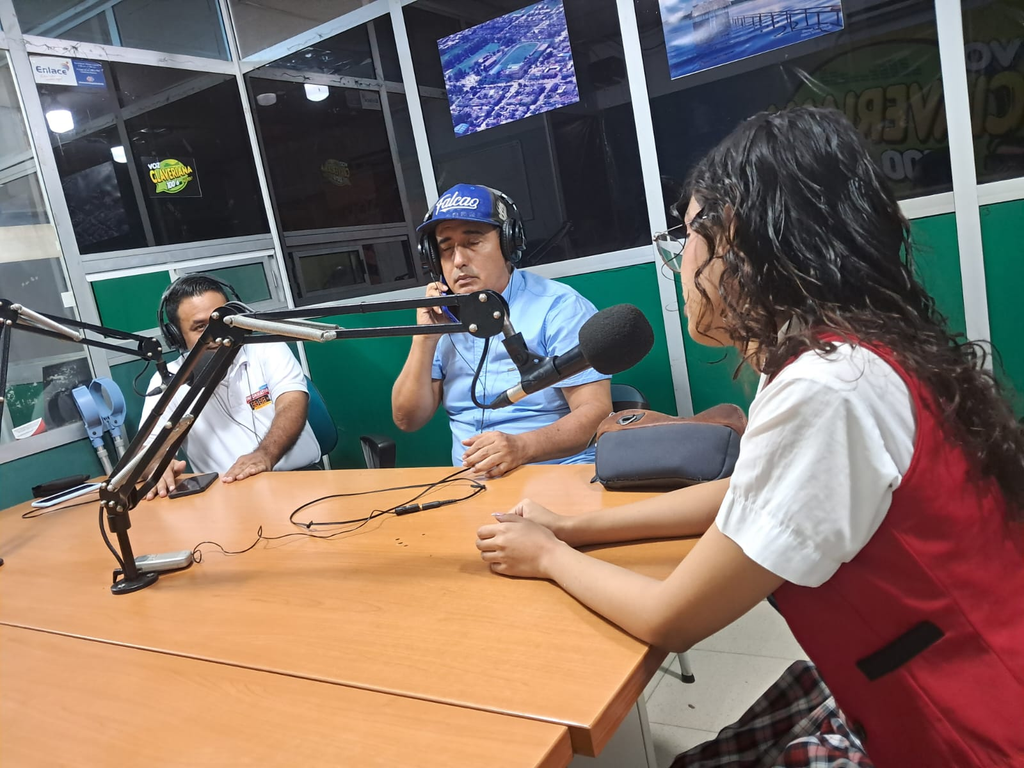 Laura Sofía Vargas Cervera participa en una entrevista en la emisora La Voz Claveriana, sentada frente a un micrófono en el estudio de radio. A su lado se encuentran dos integrantes de la emisora con audífonos y micrófonos, en un espacio de conversación sobre sus resultados en SABER 11, su proyecto de robótica y sus aspiraciones académicas y profesionales.