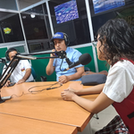 Laura Sofía Vargas Cervera participa en una entrevista en la emisora La Voz Claveriana, sentada frente a un micrófono en el estudio de radio. A su lado se encuentran dos integrantes de la emisora con audífonos y micrófonos, en un espacio de conversación sobre sus resultados en SABER 11, su proyecto de robótica y sus aspiraciones académicas y profesionales.